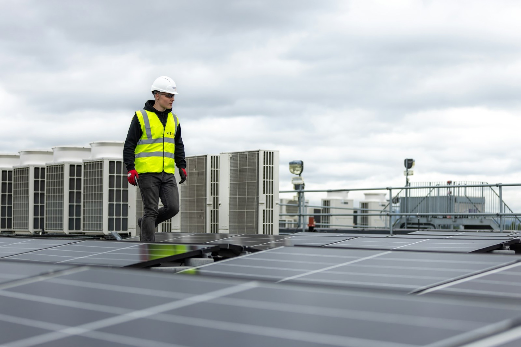 A technician walking past air conditioning units on a rooftop